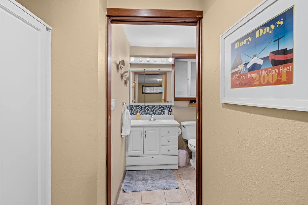 A bright bathroom featuring a white vanity with a sink, a large mirror, and a toilet. The walls are light yellow, and the floor is tiled, with a blue bath mat.