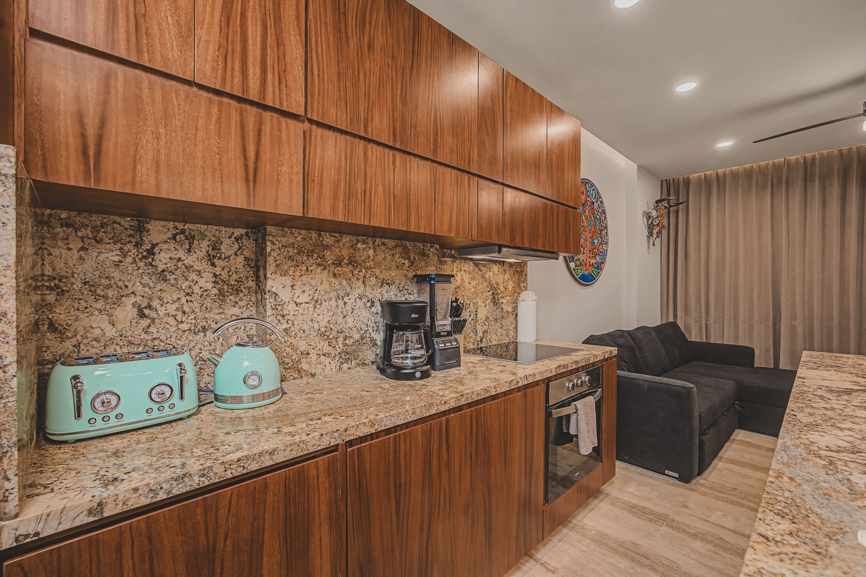 A detailed view of the kitchen counter highlights the speckled granite surface and warm wood cabinetry, featuring a sleek induction cooktop and oven. A retro-inspired turquoise toaster and kettle add a pop of color alongside a coffee maker and blender.