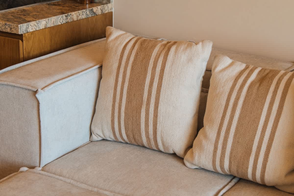 A cozy living room corner features a light beige sofa with two striped throw pillows in cream and tan. The sofa's textured fabric and clean lines contribute to a comfortable and inviting atmosphere.