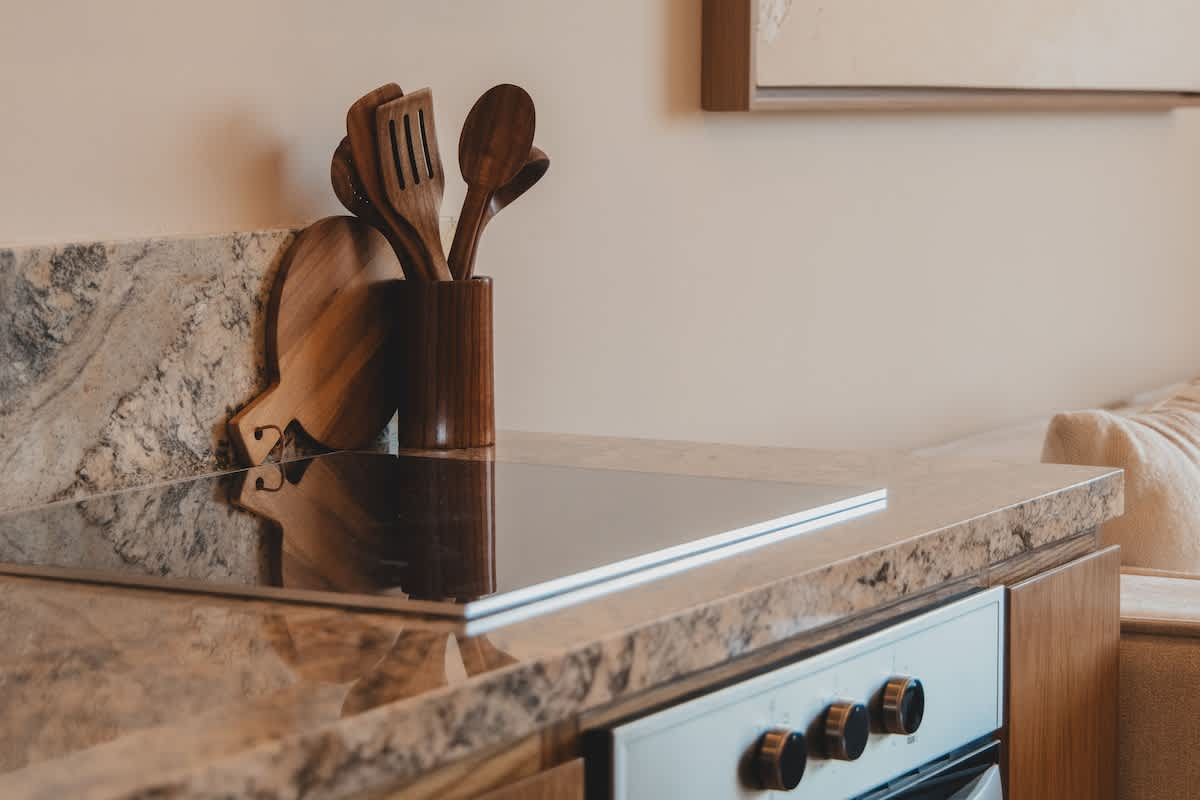 A sleek kitchen counter showcasing a black induction cooktop seamlessly integrated into a speckled granite countertop, with wooden utensils and cutting boards neatly arranged nearby.