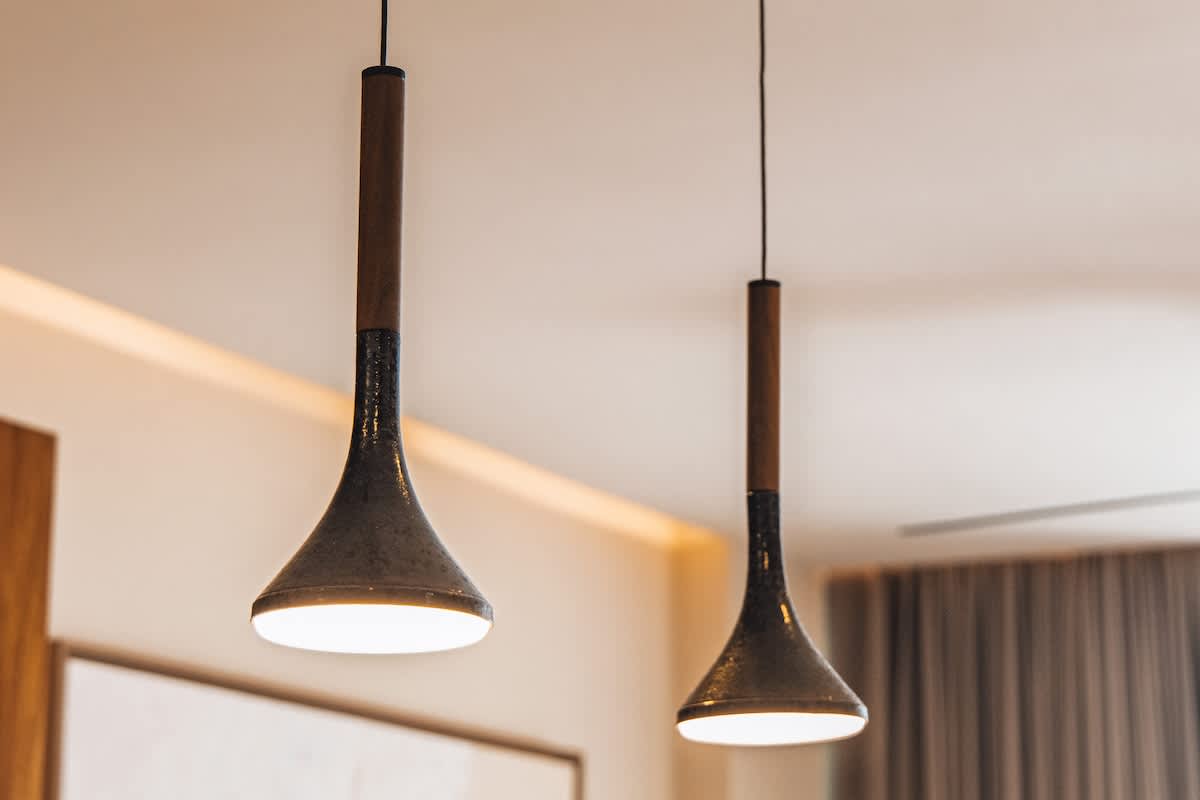 Two modern pendant lights with dark, textured bell-shaped shades and wooden accents hang from a light-colored ceiling, providing warm downward illumination.