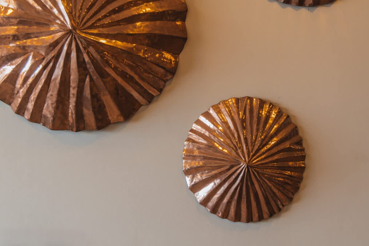 A collection of three circular, fanned copper wall art pieces of varying sizes, arranged on a light-colored wall, adding a metallic and textured decorative element.