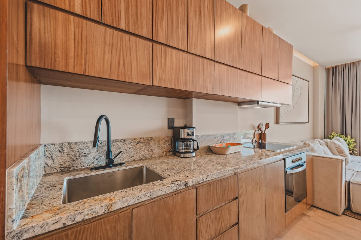 Detailed view of the modern kitchen counter featuring a stainless steel sink, black faucet, coffee maker, and a sleek induction cooktop, all set against light wood cabinetry and granite backsplash.