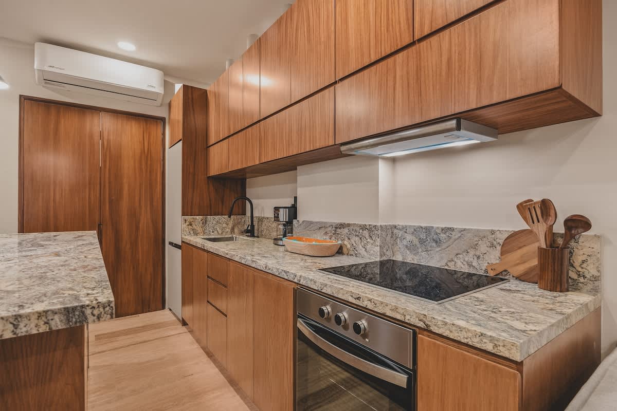 Contemporary kitchen counter with speckled granite, a built-in induction cooktop, and a stainless steel oven, surrounded by warm wood cabinetry and a modern range hood.