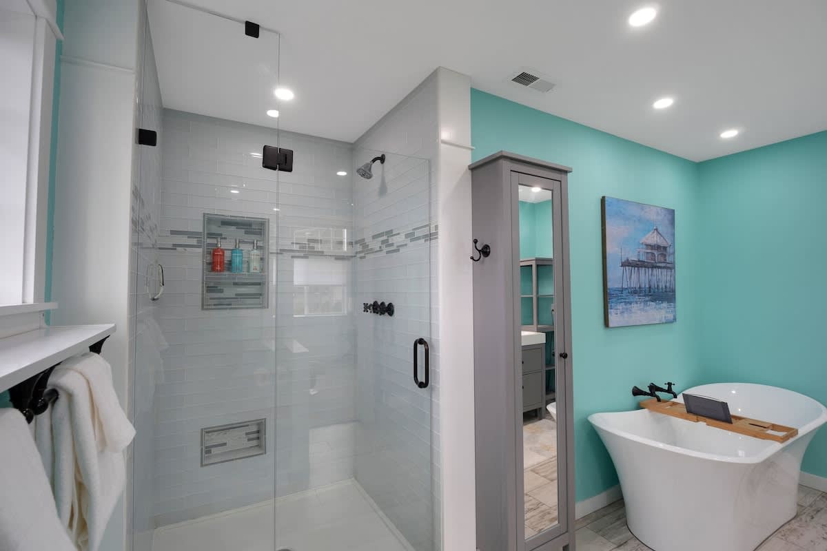 The modern glass-enclosed shower in the teal-walled bathroom, featuring light blue subway tiles with a decorative accent band and black fixtures.