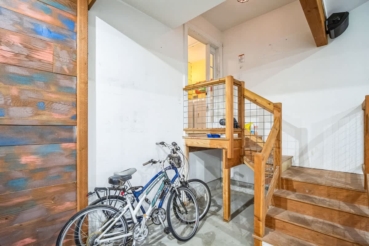 A functional garage space features wooden stairs leading to an upper level, two bicycles stored against a wall with rustic wood paneling, and a unique wooden enclosure with wire mesh.