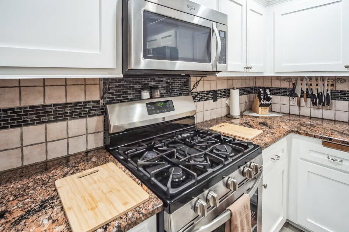 Close-up of a stainless steel gas range with a matching over-the-range microwave, set against a tiled backsplash with decorative black accents and speckled granite countertops.
