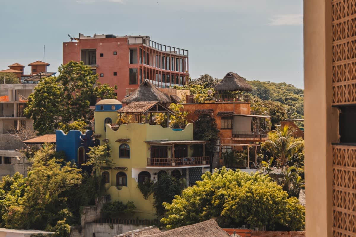A vibrant hillside view showcasing an array of colorful buildings with unique architectural styles, nestled among dense green trees under a bright, clear sky, offering a panoramic townscape.