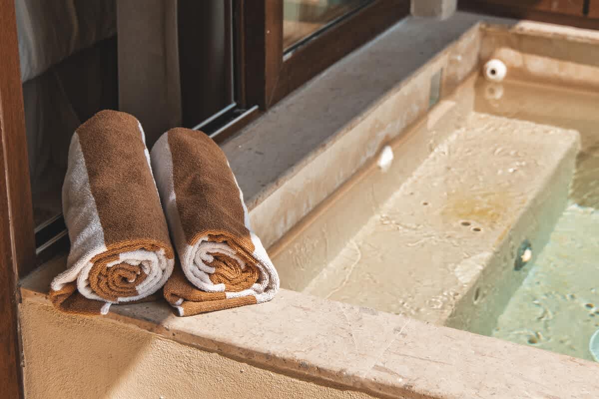 A close-up view of a built-in hot tub on a patio, with two brown and white striped towels neatly rolled and placed on the stone ledge beside the inviting water.