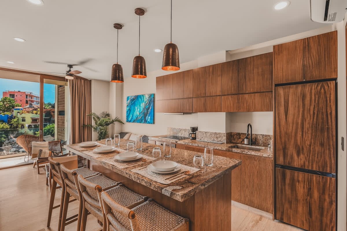 Modern kitchen with dark wood flat-panel cabinetry, granite countertops, and a large island with bar seating, equipped with stainless steel appliances and offering an open view to the living area.