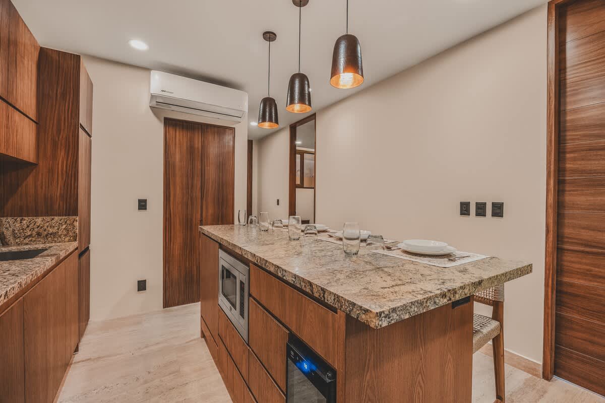 Contemporary kitchen featuring dark wood cabinetry, granite countertops, and a large island with integrated microwave and wine cooler, illuminated by three pendant lights.