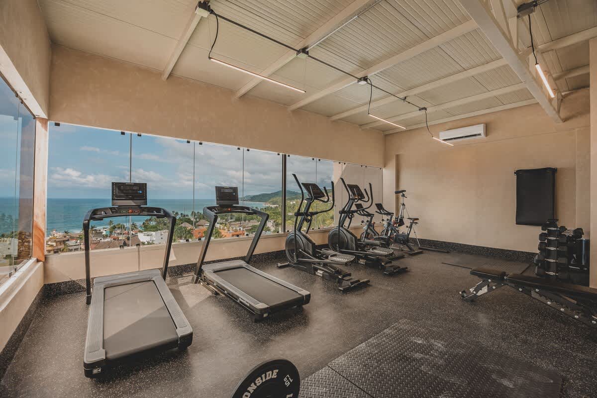 Cardio machines, including treadmills and ellipticals, are neatly arranged in the gym, providing users with an inspiring view of the blue ocean and the bustling coastal town through a wide glass wall.