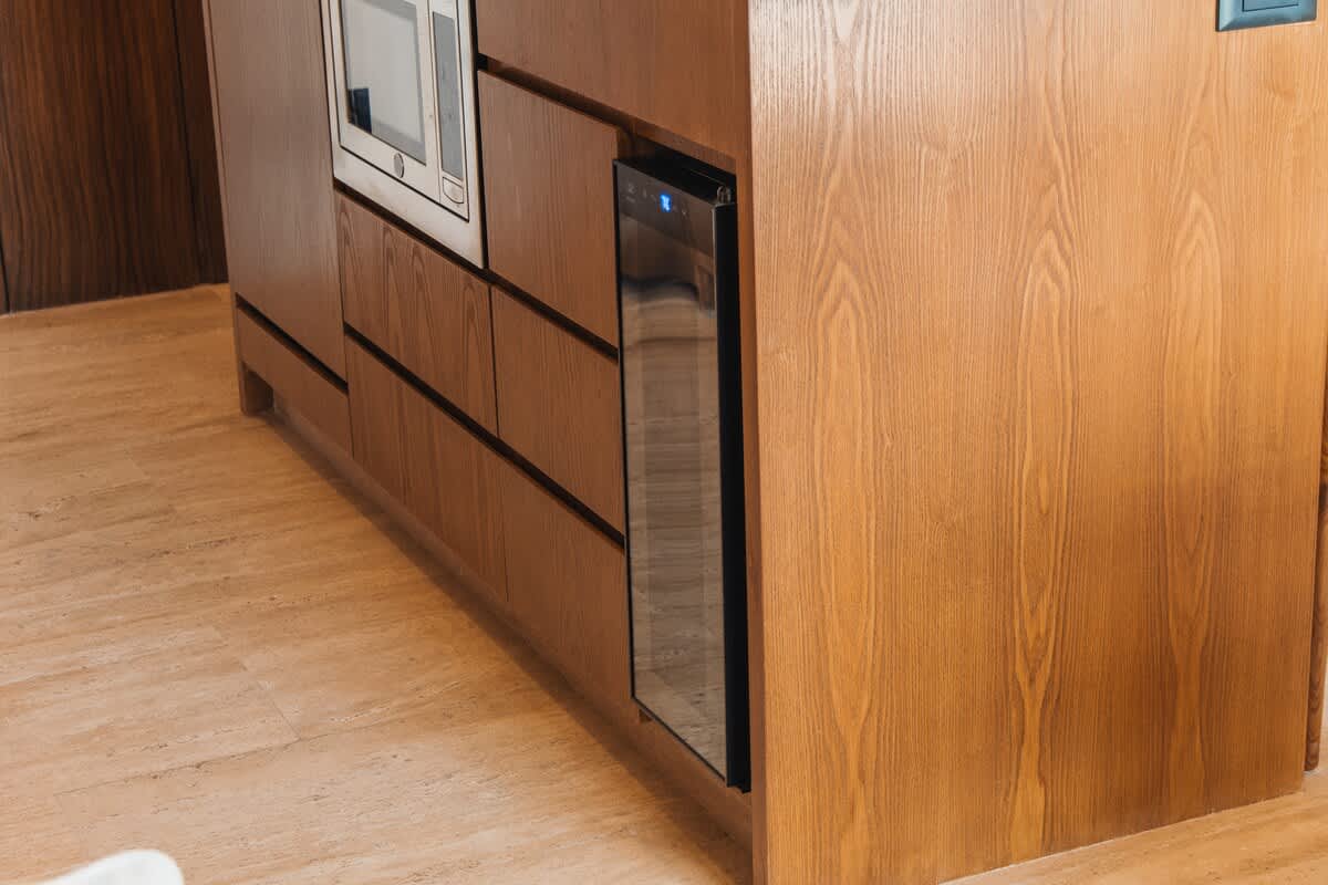 A built-in wine cooler with a glass door is integrated into light wooden kitchen cabinetry, next to a microwave, showcasing modern and functional kitchen design.