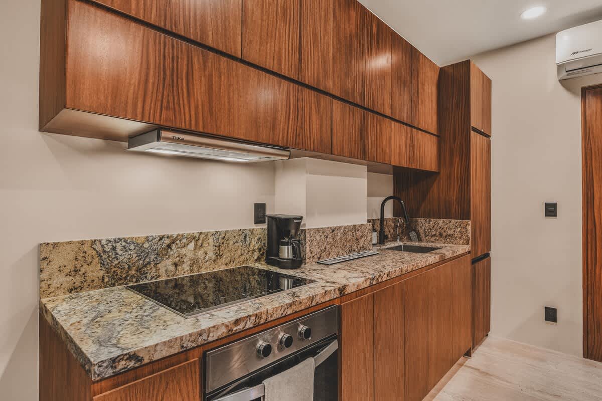 Modern kitchen with dark wood flat-panel cabinets, speckled granite countertops, and a built-in electric cooktop and oven, featuring a black faucet and under-cabinet lighting.
