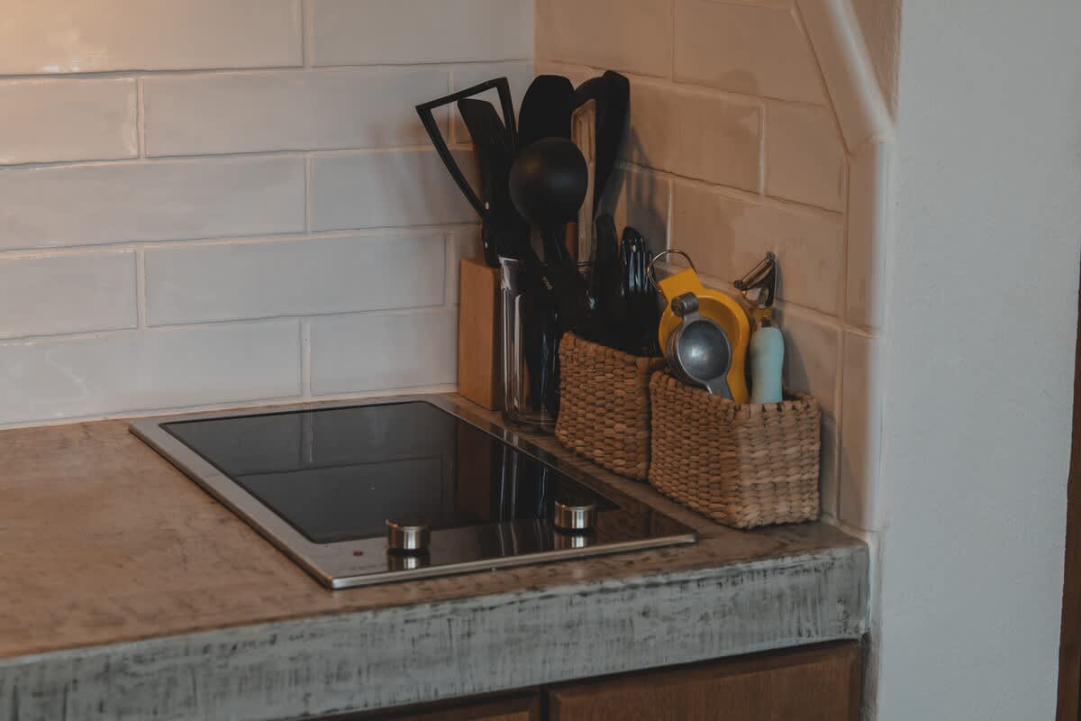 Modern kitchen countertop with a sleek built-in electric stovetop and white subway tile backsplash. Various cooking utensils are neatly organized in wicker baskets and a wooden holder.