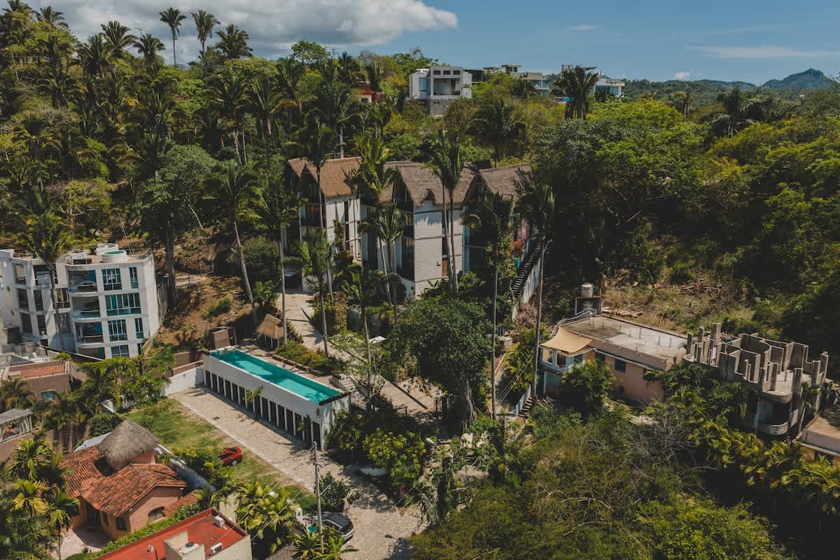Expansive aerial view of the property and its surroundings, showing the main buildings with thatched roofs, a long swimming pool, and other residential structures nestled within a vast, green tropical landscape.
