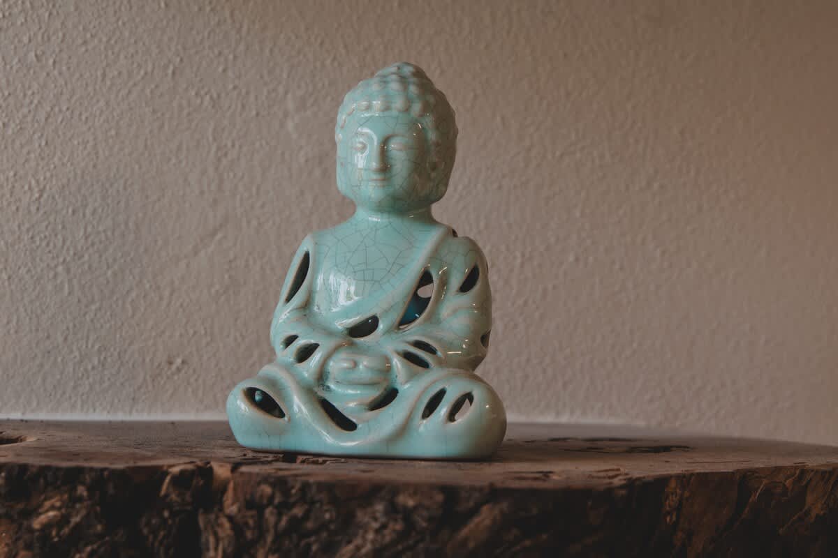 A serene light blue ceramic Buddha statue, featuring intricate cutouts and a crackled glaze, rests on a textured, rough-hewn wooden surface, adding a tranquil decorative element.