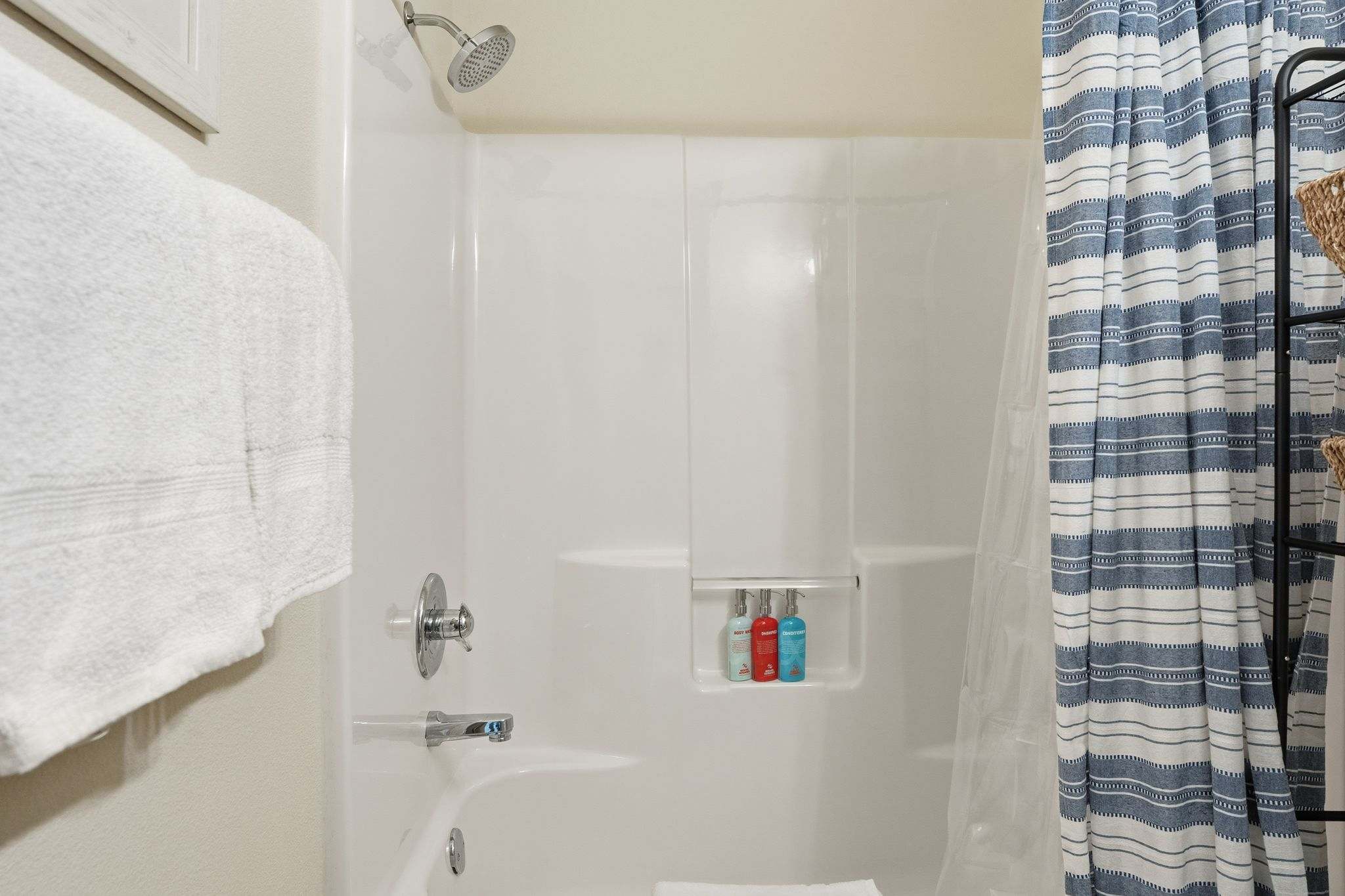 Close-up of a white tub/shower combo featuring a chrome shower head and faucet. A built-in niche holds three eco-friendly bottles of body wash, shampoo, and conditioner.
