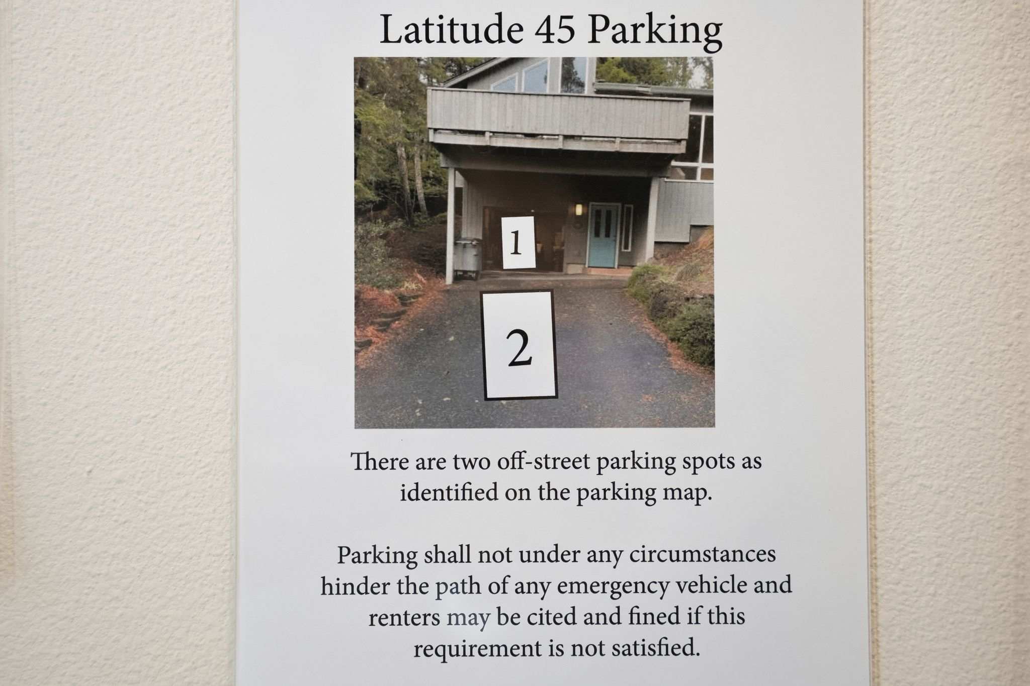 A framed sign displays "Latitude 45 Parking" with an image of the property's exterior, highlighting two numbered off-street parking spots. Text below details parking regulations and potential fines.