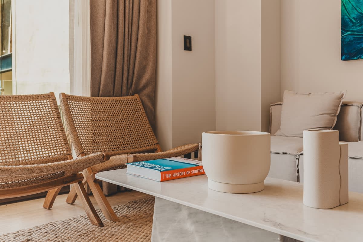 A cozy living area featuring two natural woven rattan chairs, a white marble coffee table with decorative objects, and a light-colored sofa, all set on a textured rug.