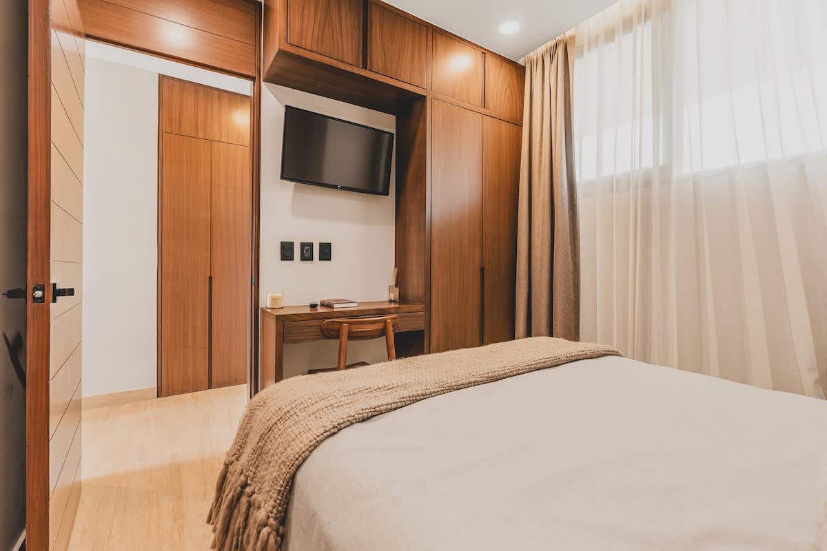 Second bedroom featuring a bed with light bedding, a wall-mounted television above a small wooden desk and chair, and extensive built-in wooden cabinetry.