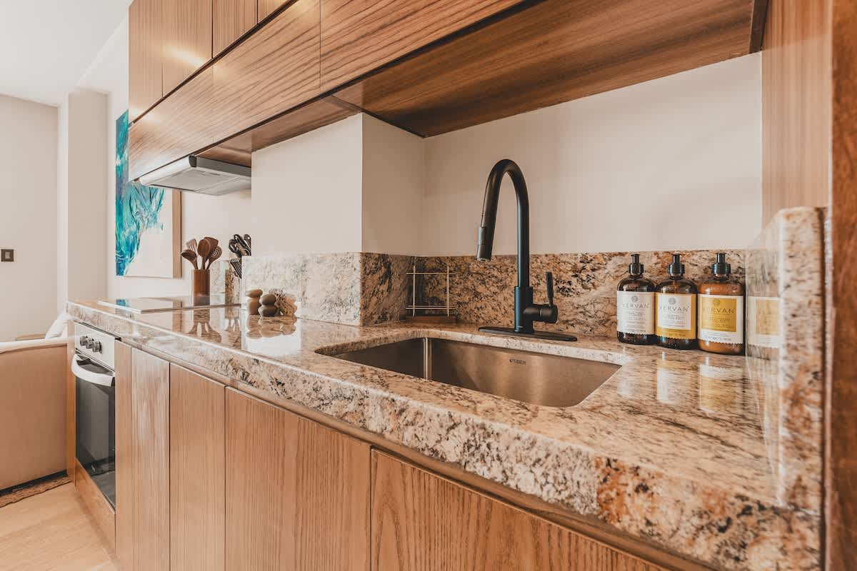 The kitchen showcases a stainless steel sink with a modern black gooseneck faucet, set into a speckled granite countertop. Wooden cabinetry provides ample storage, and decorative soap dispensers are visible on the counter.
