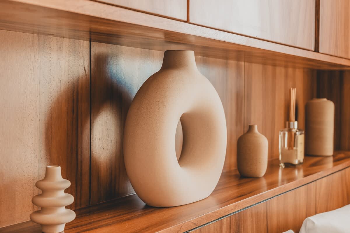 A close-up of a wooden shelf displaying a collection of minimalist ceramic vases in various shapes and sizes, alongside a reed diffuser, adding a touch of modern decor.