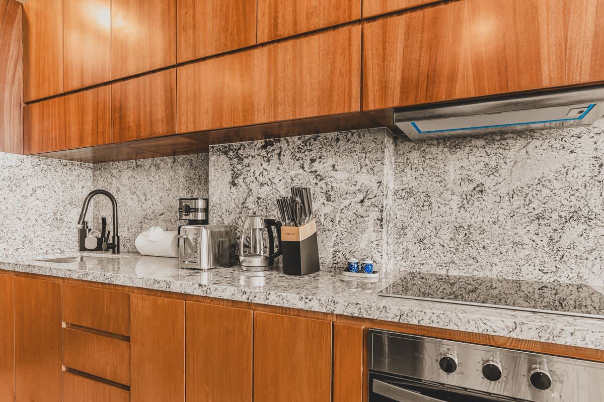 Modern kitchen featuring rich wooden upper and lower cabinets, speckled granite countertops, and stainless steel appliances including a toaster, kettle, and built-in oven.