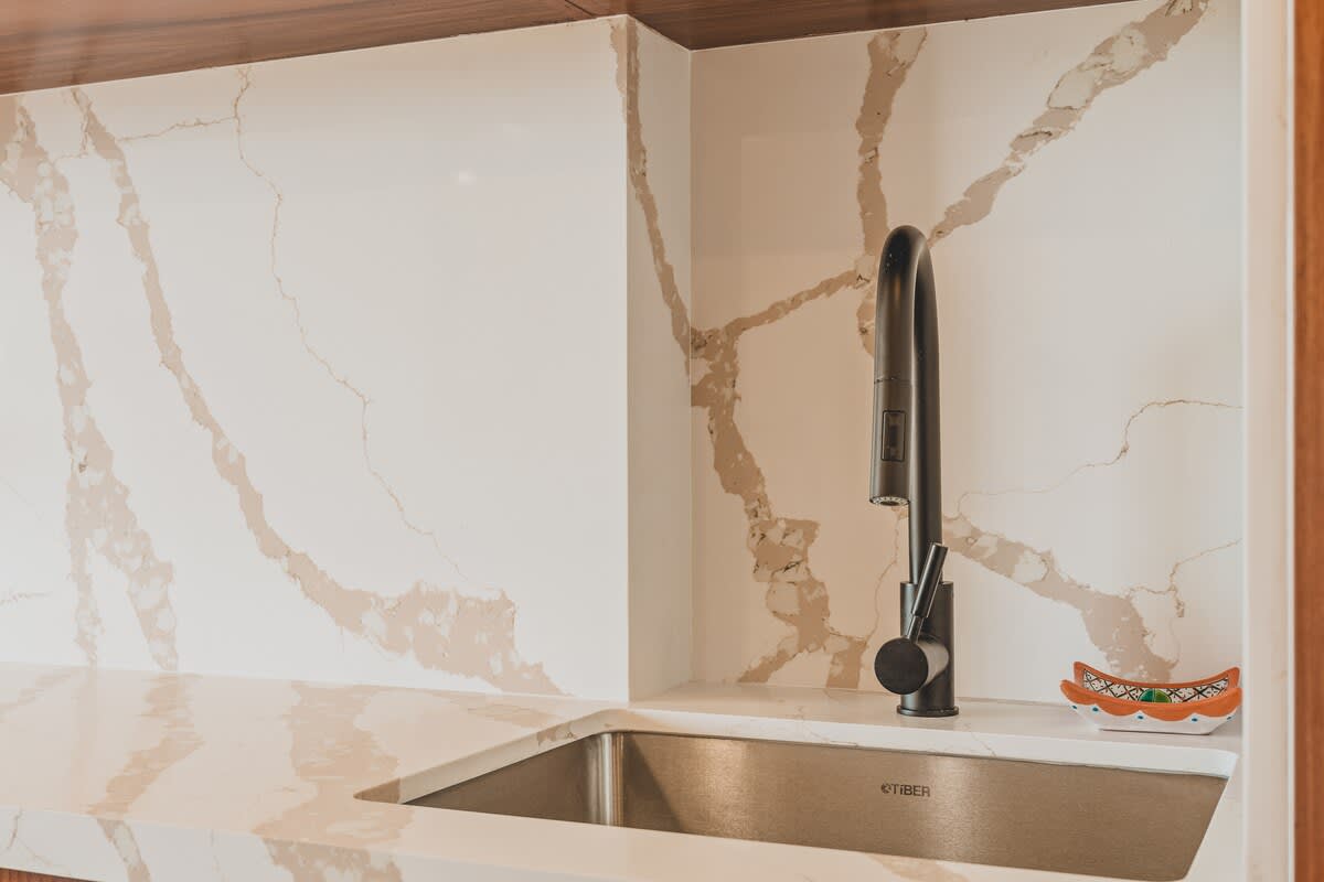A detailed view of the kitchen sink area, highlighting the modern matte black gooseneck faucet and the striking grey veining of the white quartz countertop and backsplash. A small decorative dish sits by the sink.
