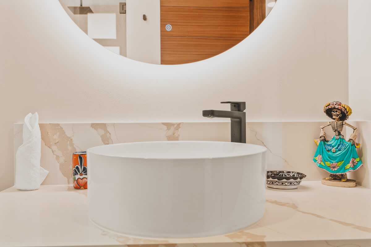 A contemporary bathroom vanity showcases a white cylindrical vessel sink, a sleek black faucet, and a light marble countertop, complemented by a vibrant ceramic cup and a festive skeleton figurine.