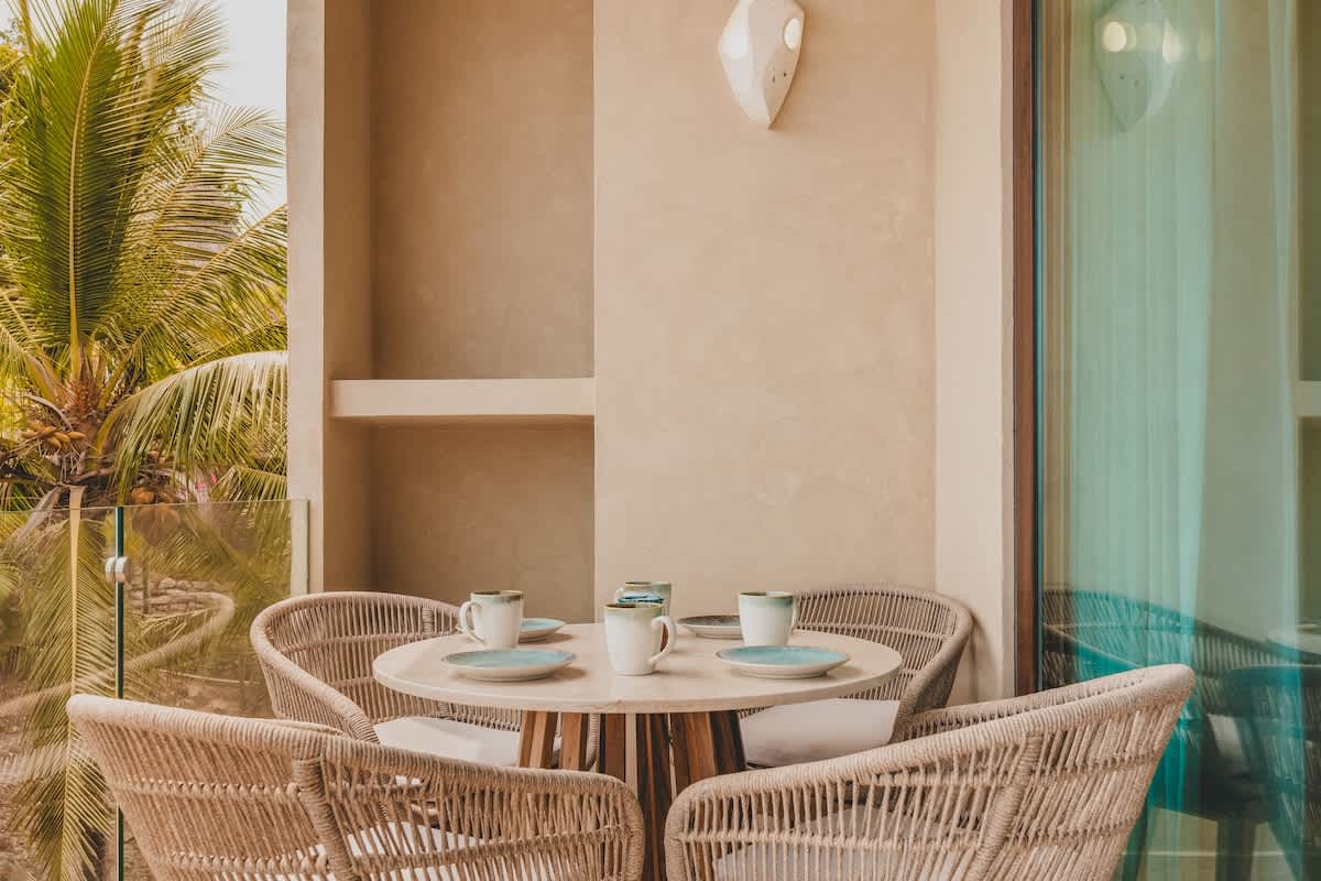 Outdoor balcony featuring a round dining table with four woven chairs, set against a backdrop of lush palm trees, perfect for al fresco dining.