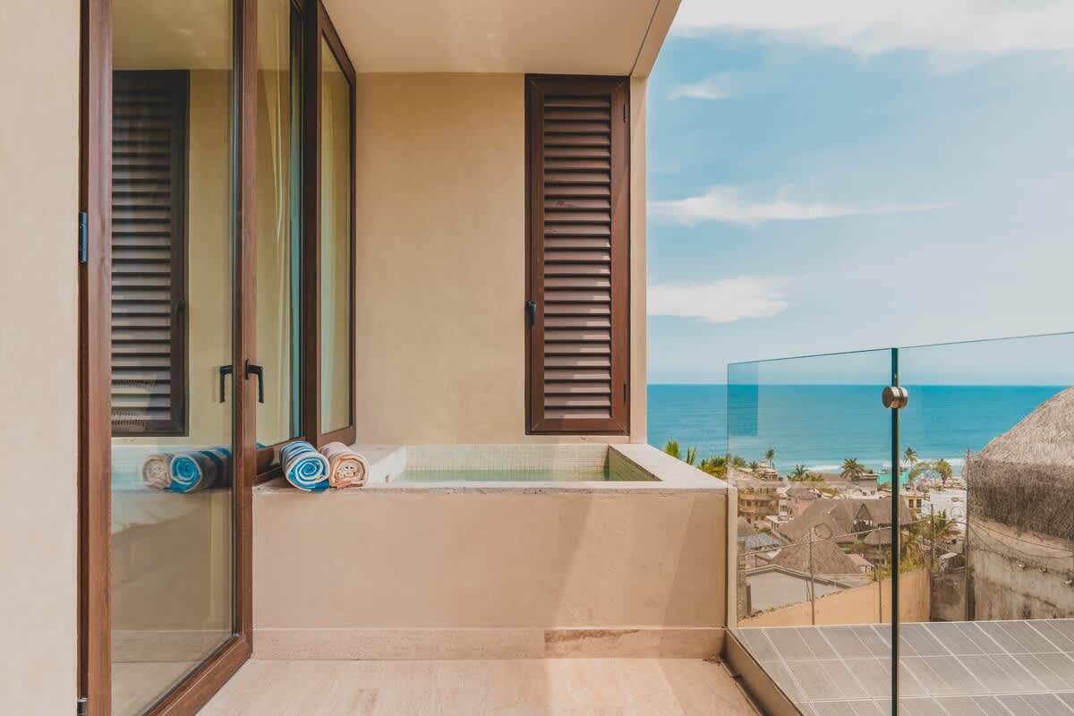 Private balcony with a small plunge pool, featuring a glass railing for unobstructed views of the ocean and the coastal town, with rolled towels neatly placed by the pool.