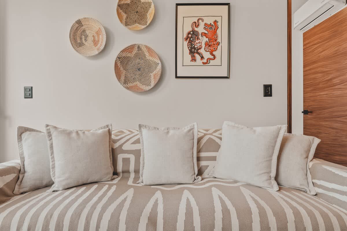 Close-up of the living room sofa adorned with light pillows and a patterned blanket, complemented by a wall decorated with three woven baskets and a framed artwork depicting two stylized tigers.