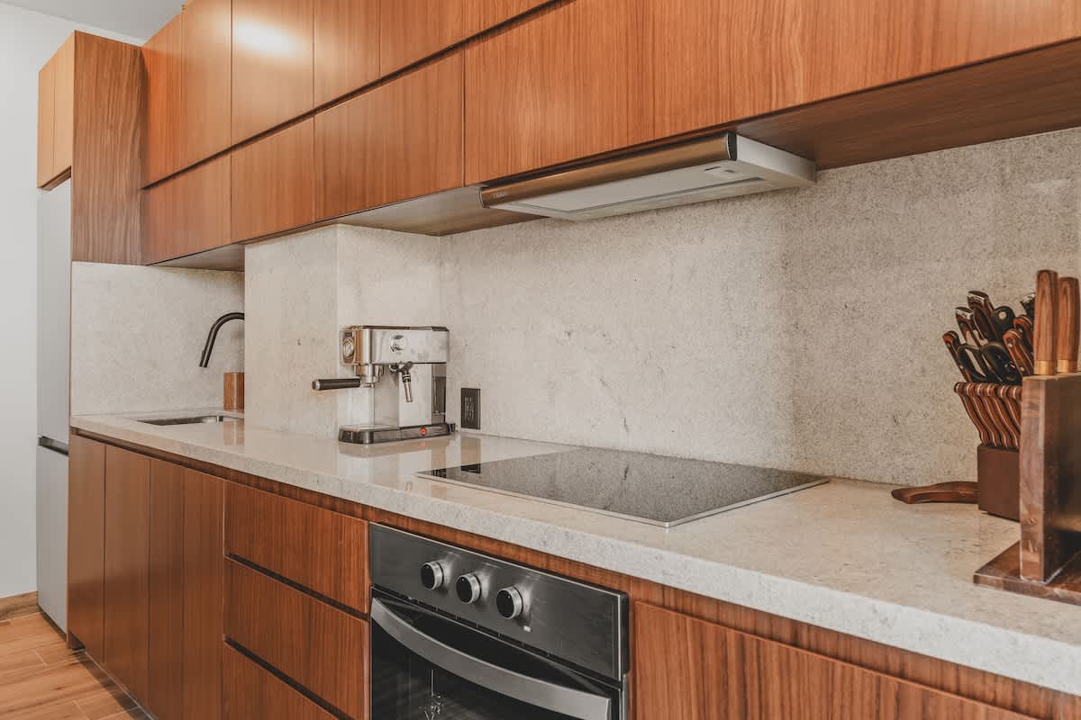 Detailed view of a modern kitchen counter with light stone backsplash, featuring a sleek black faucet over a stainless steel sink, an espresso machine, and an induction stovetop above a built-in oven.