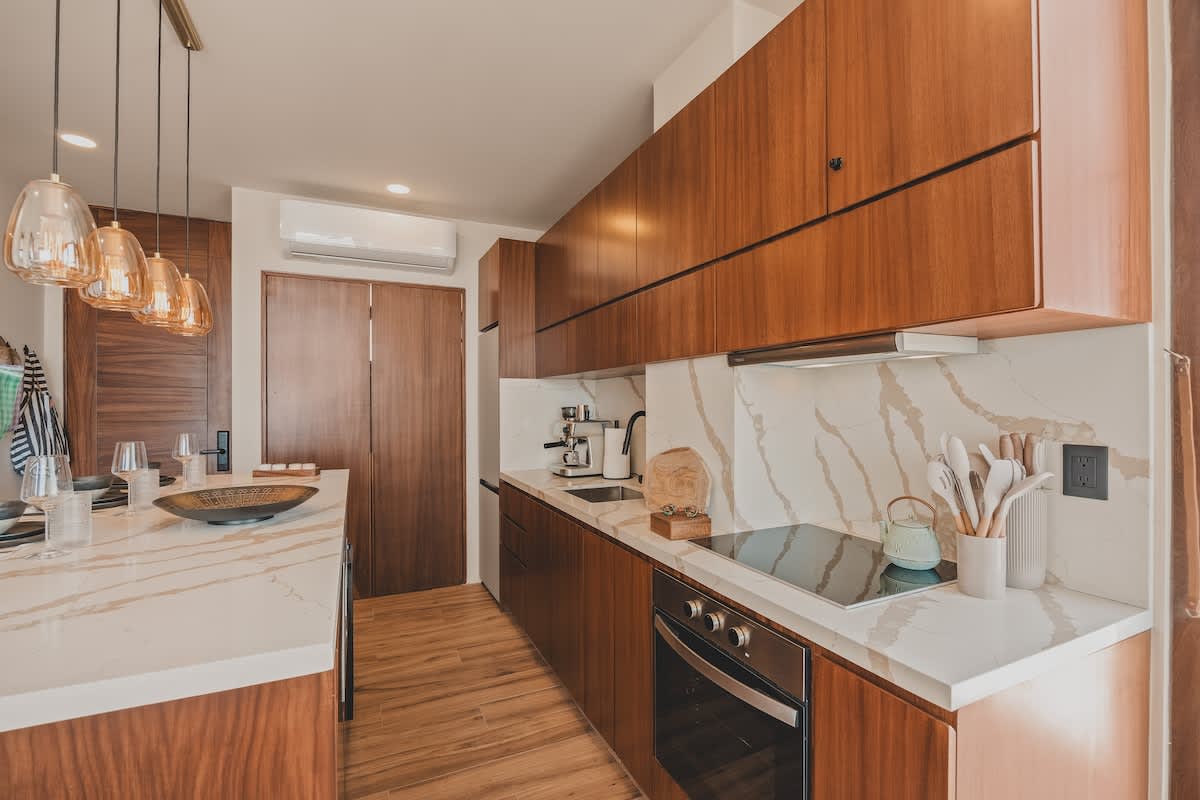 Contemporary kitchen featuring rich wood cabinetry, white marble countertops and backsplash with prominent veining, and integrated appliances including a stovetop and oven, with a view towards a dining area.
