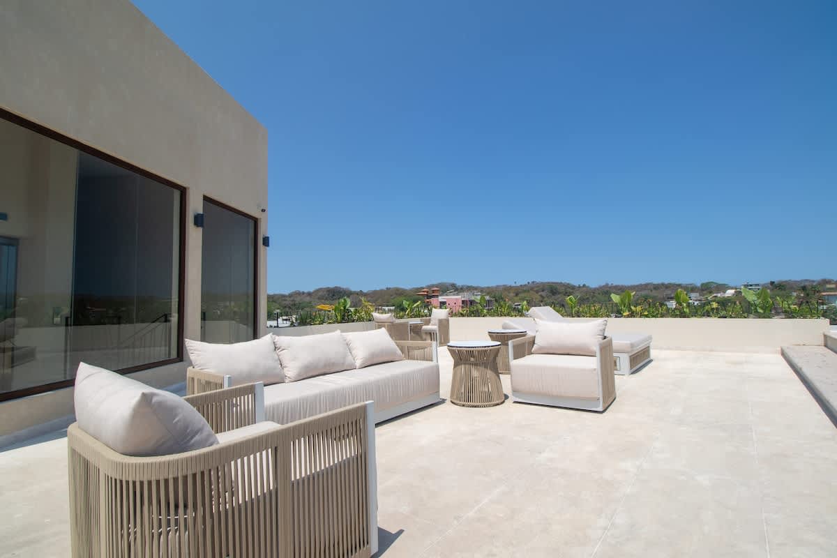 Spacious rooftop deck with contemporary outdoor lounge furniture, including sofas and armchairs with light cushions, set against a minimalist building facade under a clear blue sky.