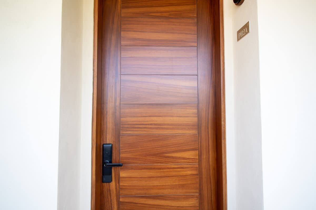 A sleek, modern wooden entrance door with horizontal paneling and a black handle is set into a clean white wall, featuring a small "P12A" plaque indicating a unit number.