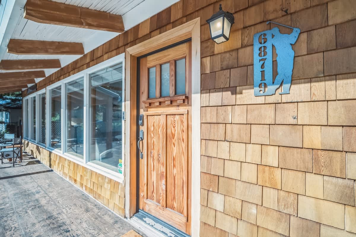 Front entrance of a house with cedar shake siding, a natural wood door with glass panels, and a decorative golf-themed house number sign.