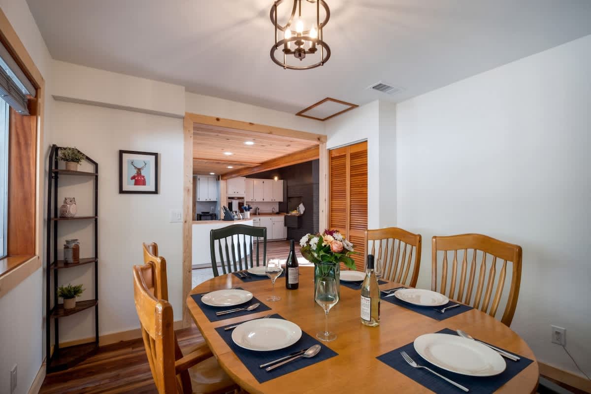 Dining area looking towards the kitchen, showing an open doorway with wood trim, a black metal shelving unit, and a framed deer artwork, with the oval dining table in the foreground.