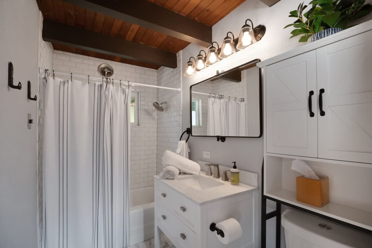 Modern bathroom with white subway tile shower, dark wood ceiling beams, a white vanity with a marble-look countertop, and a large rectangular mirror.