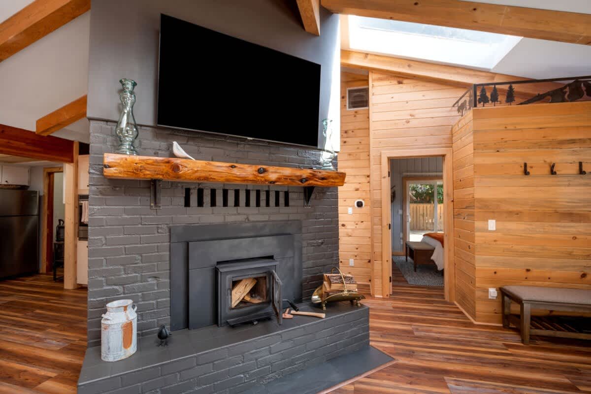 A detailed view of the living room's dark gray brick fireplace, featuring a wood-burning stove insert and a rustic wooden mantelpiece with a large TV mounted above. Wooden paneling is visible to the right.