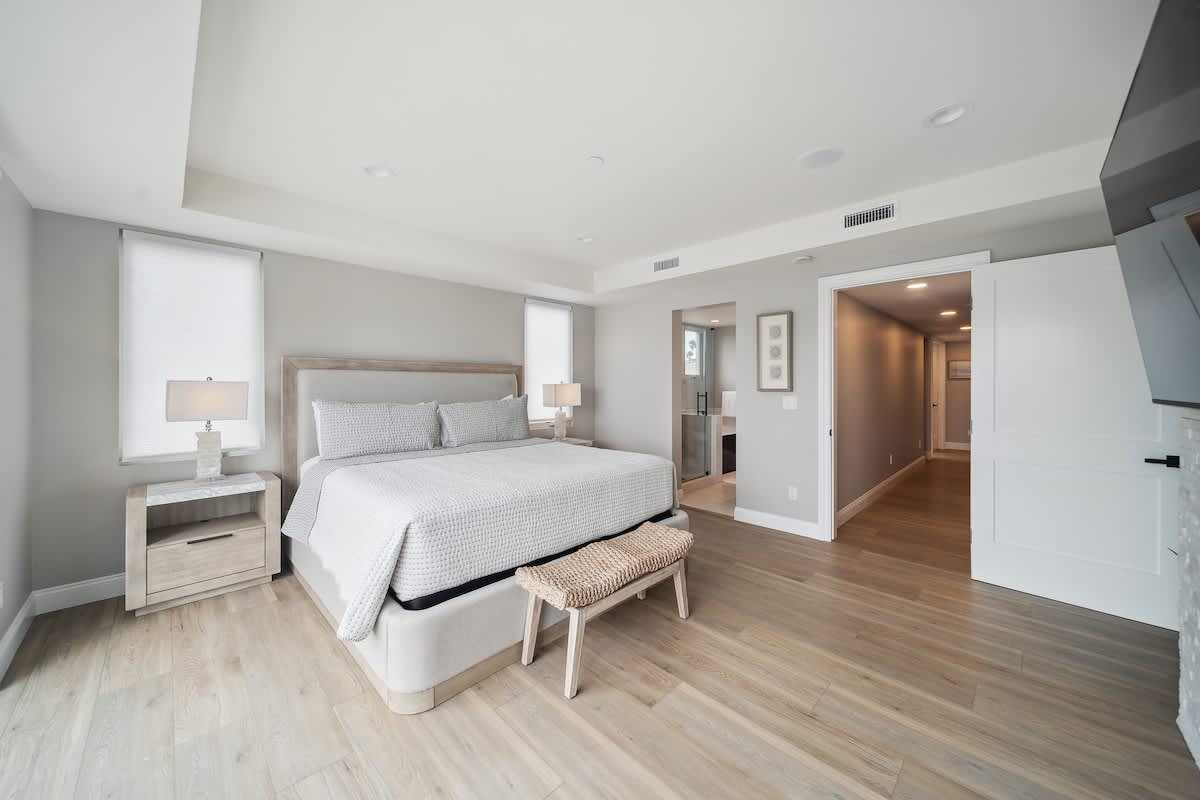 Spacious bedroom with light wood floors, a large bed, and an open doorway leading to an ensuite bathroom with a glass shower and separate tub.