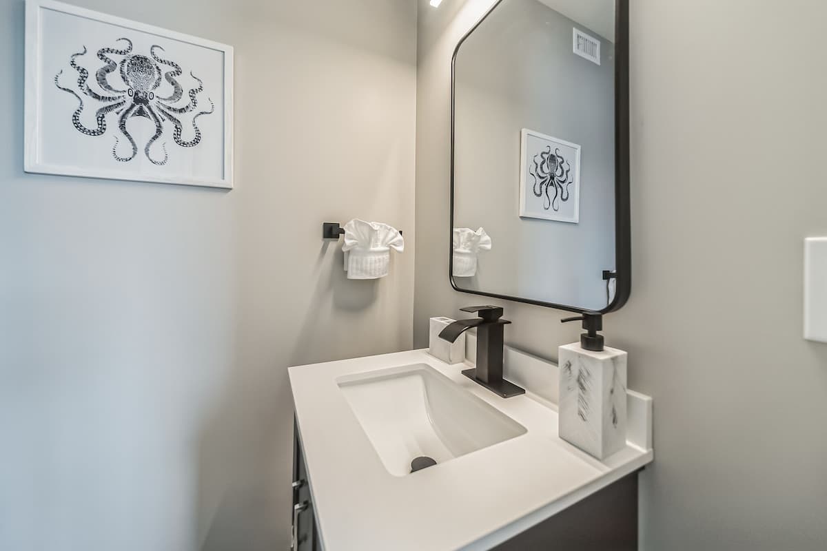 Contemporary powder room with a white vanity, black faucet, rectangular mirror, and a framed black and white octopus print on a light gray wall.