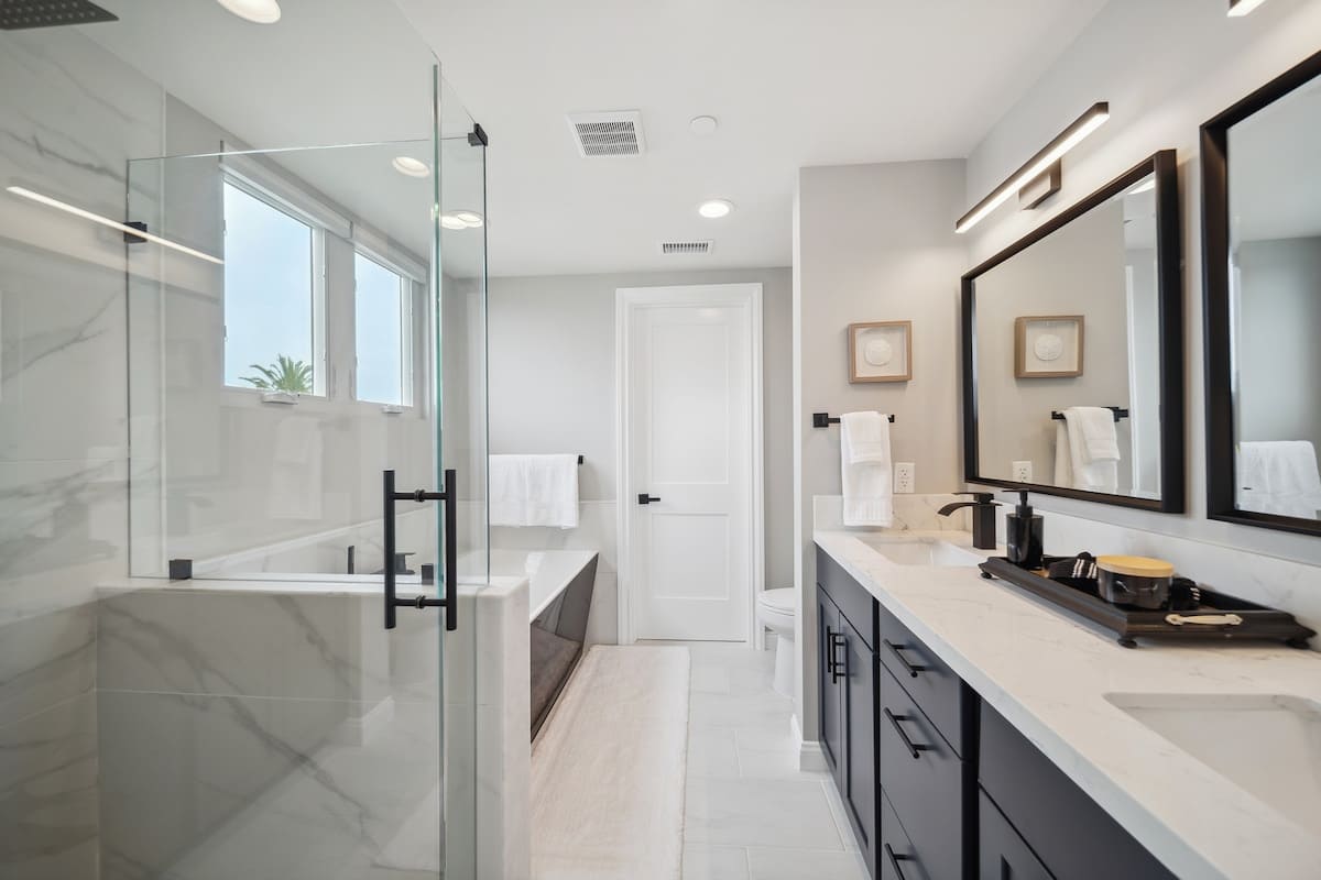 Modern bathroom with a double vanity featuring dark cabinets and white countertops, a glass-enclosed shower, and a separate soaking tub.