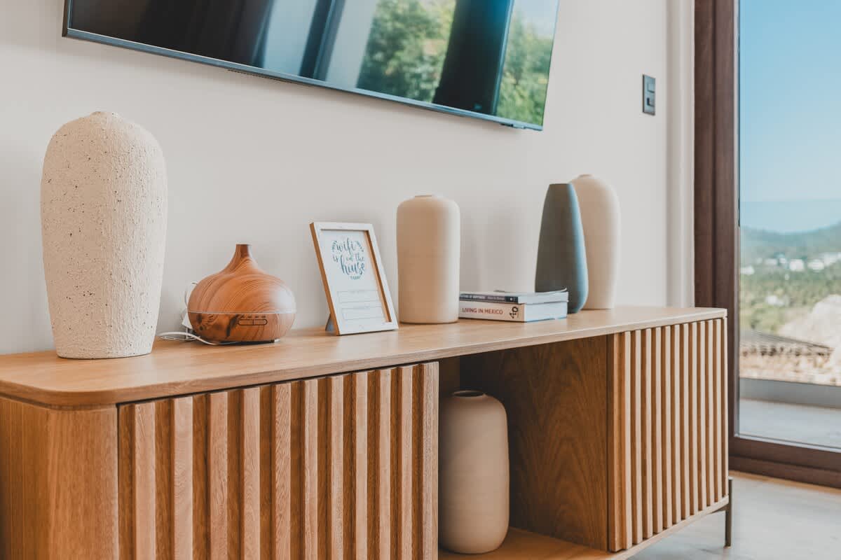 Stylish living area featuring a slatted wooden console table adorned with various decorative vases, an essential oil diffuser, and a wall-mounted television above.