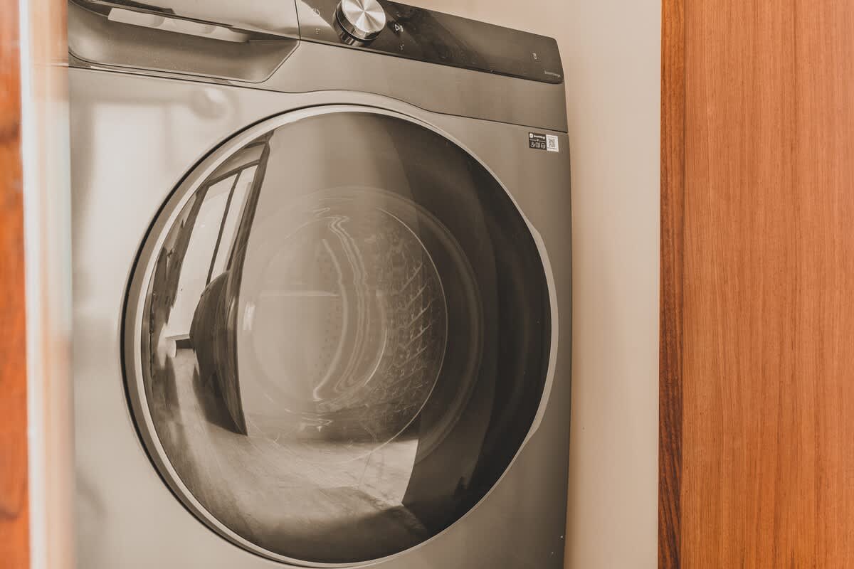 Close-up view of a modern front-loading washing machine with a dark finish, featuring a large circular glass door, set against a light wall next to a wooden door frame.