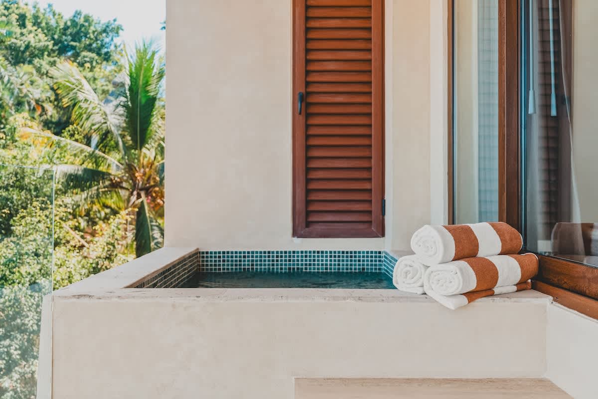 Detailed view of the balcony's built-in plunge pool, showcasing blue mosaic tiles and neatly folded white and brown striped towels, set against a backdrop of lush tropical trees.