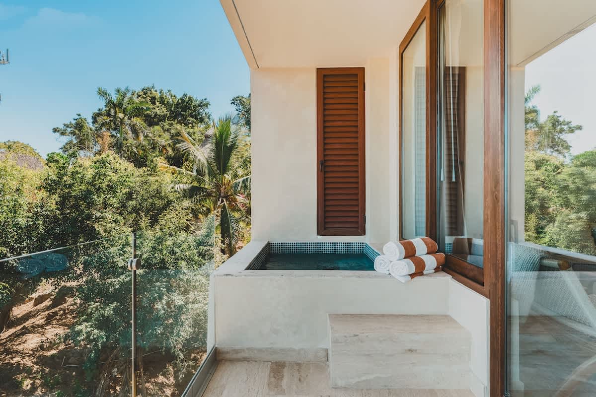 Private balcony featuring a built-in plunge pool or hot tub with blue mosaic tiles, neatly stacked towels, and surrounded by lush tropical greenery.