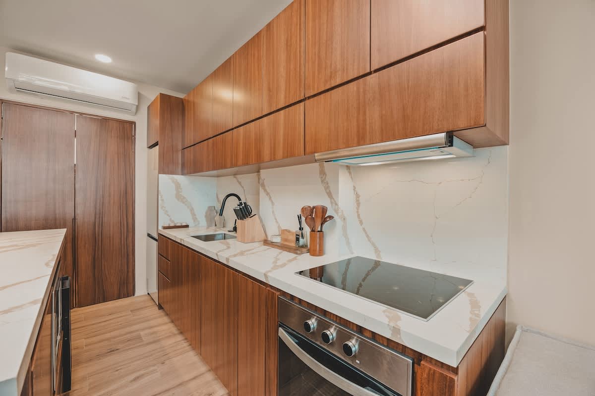 Modern kitchen counter with dark wood lower cabinets, white marble countertops, an electric stovetop, and an integrated oven, with a stainless steel range hood above.