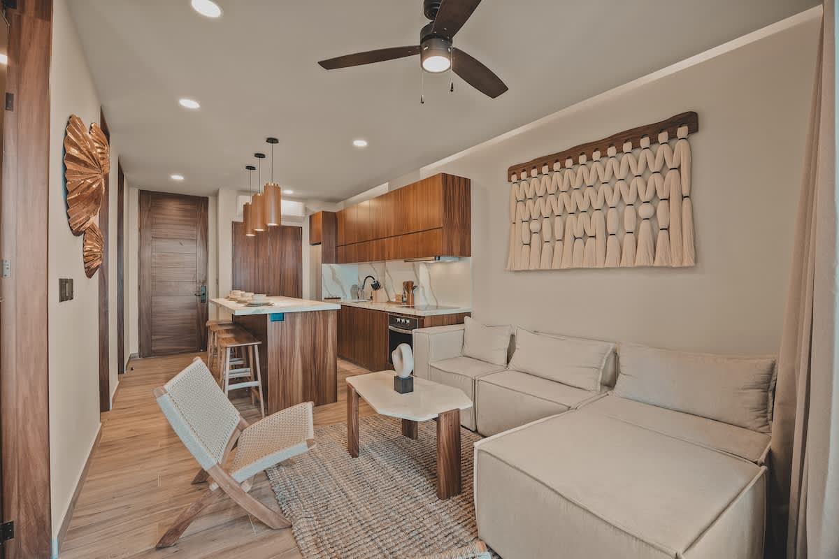 Cozy living room with a light-colored sectional sofa, a coffee table, and a woven rug, open to the modern kitchen with wood cabinetry and a marble island.